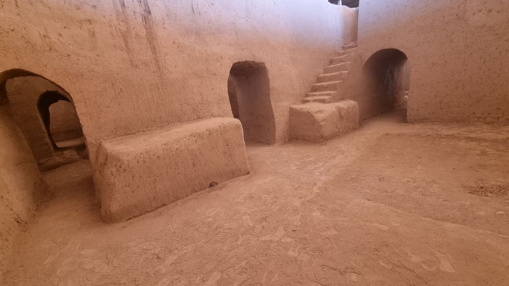 A red-clay space with arched doorways opening on to it and a staircase as well.