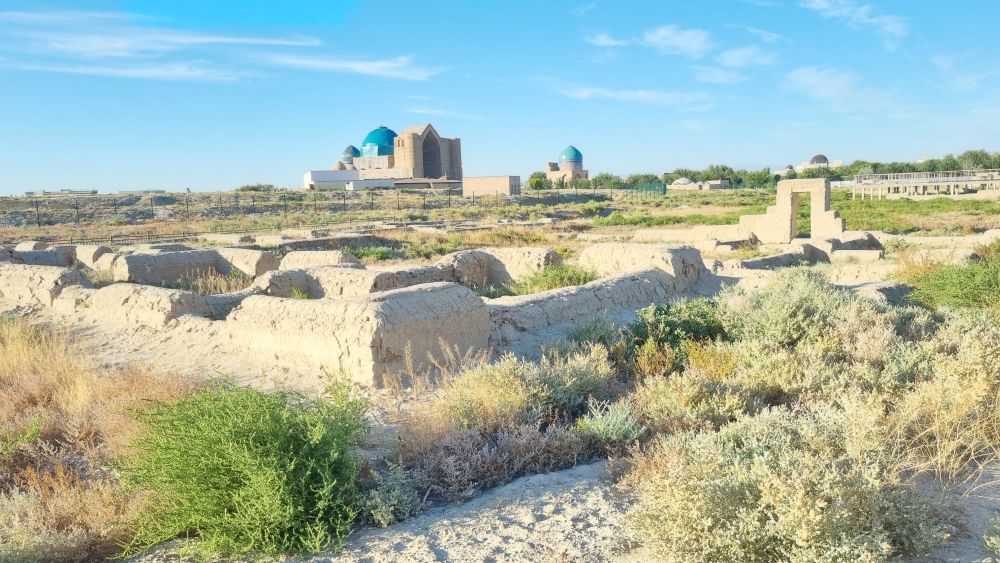 A view across a field with low walls outlining buildings, and the mausoleum in the distance.
