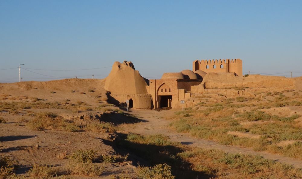 A bumpy sandy landscape with a brick gateway and partial tower.