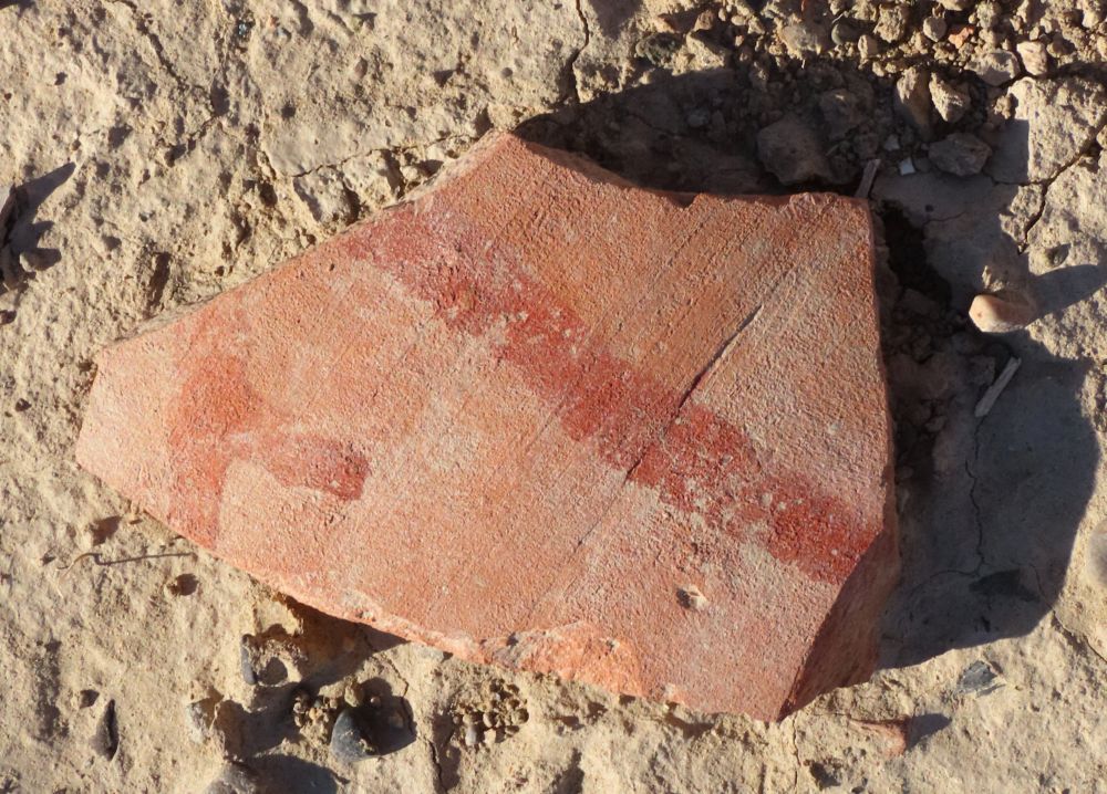 A piece of pottery with a red stripe painted across it.